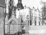 (24/48): Klasztor O.O. Franciszkanów-Reformatów<br>fot. n.n., XIX/XX w.<br>Widok klasztoru od pn.-wsch., wykonany ze zbiegu ulic Brzeskiej z ulicą przedmiejską. Na pierwszym planie mur obwodowy cmentarza przyklasztornego, z neogotycką bramą z 1860 r.W narożniku cmentarza widoczna karawaka (ob. umieszczona na zewnątrz prezbiterium kościółka). Na drugim planie dobrze widoczna północna część kościoła (do połowy okien) przed jej przebudową, wg planów A. Olszakowskiego i J. Wojciechowskiego w 1913 r.