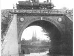(11/12): Most kolejowy fot. n.n.<br>pocz. XX w. <br>Widok mostu kolejowego z 1862 r, W tle park miejski i bazylika katedralna. Na moście lokomotywa.
